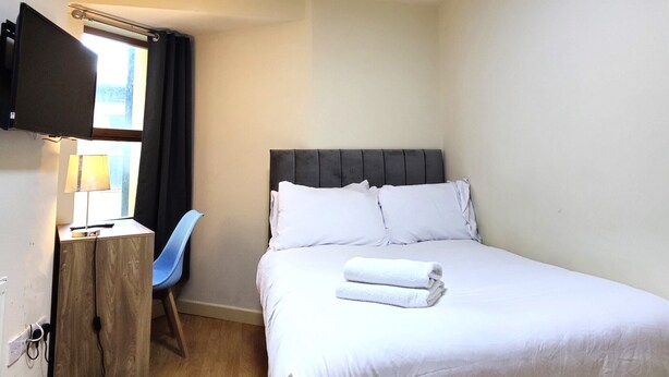 A hotel room with a bed, a desk with a lamp, a chair, and a TV mounted on the wall. - Liverpool Stays - City Centre Rooms (Liverpool)