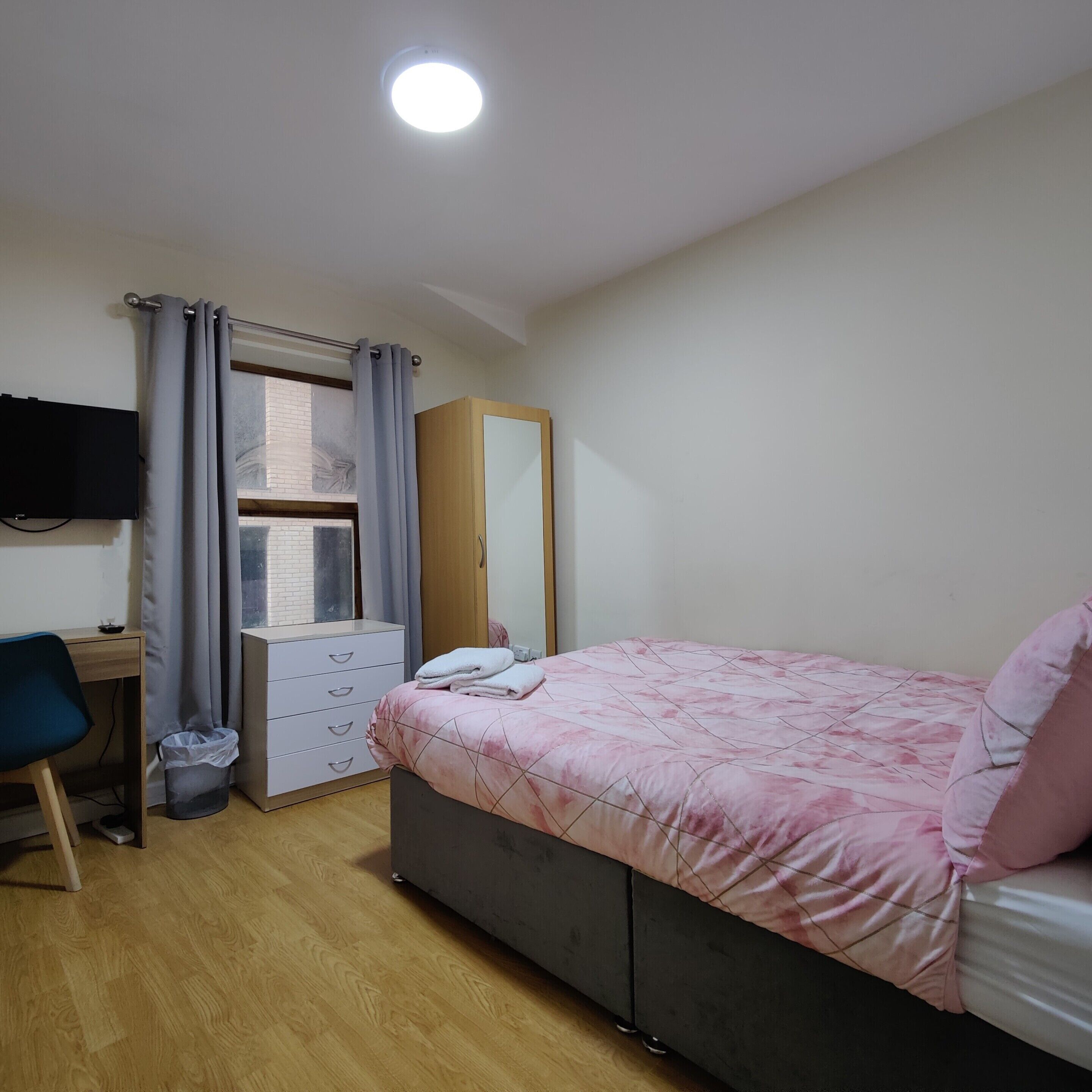 A bedroom with a bed, a desk, a chair, a wardrobe, and a window.