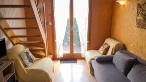 A room with a wooden staircase, a sofa, a chair, and a television.