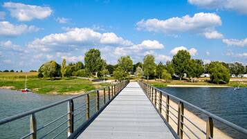 A long, flat bridge over a river with a metal railing, surrounded by trees and a clear sky.