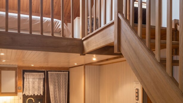 A loft-style room with a wooden staircase, a dining table with chairs, a bench, and a kitchen area with a sink and cabinets.