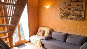 A wooden interior with a sofa, a bed, a wall-mounted light, and a window.