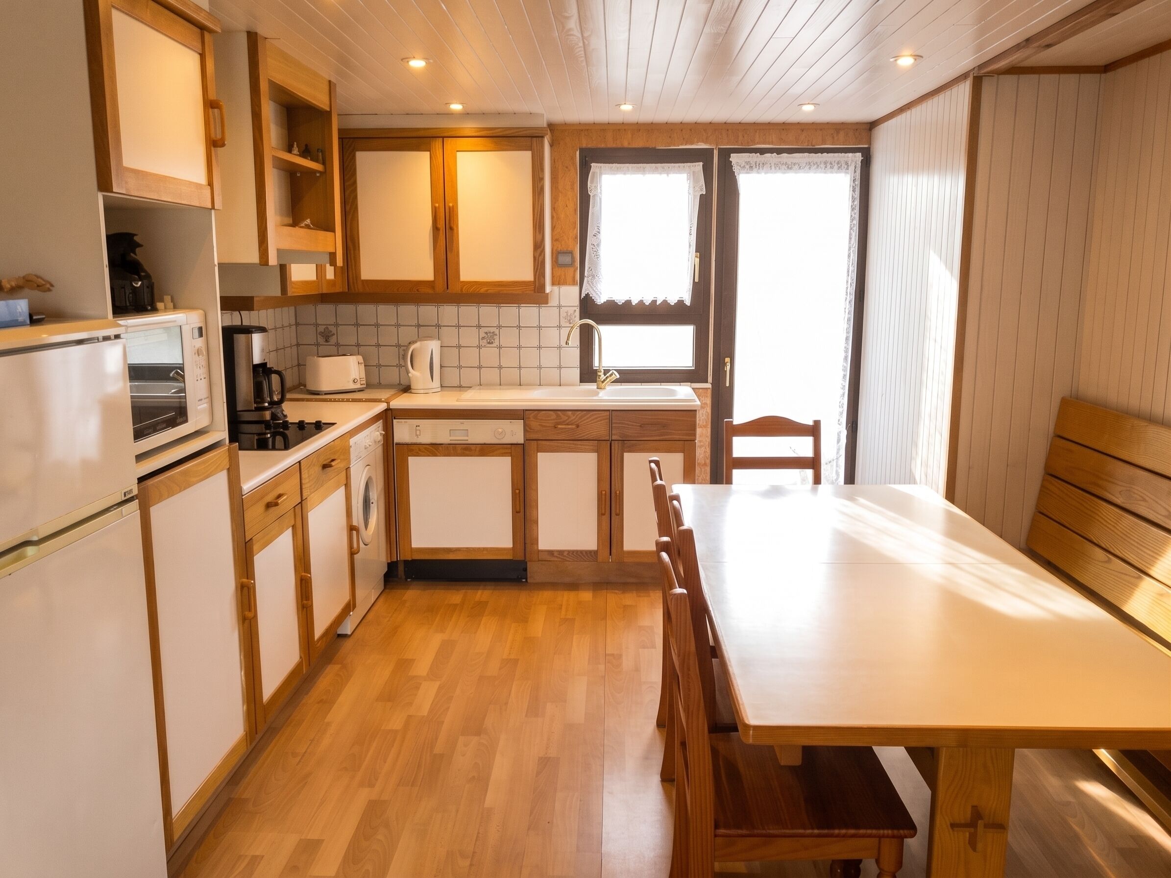 A kitchen with wooden cabinets, a sink, a dishwasher, and a dining table with chairs.