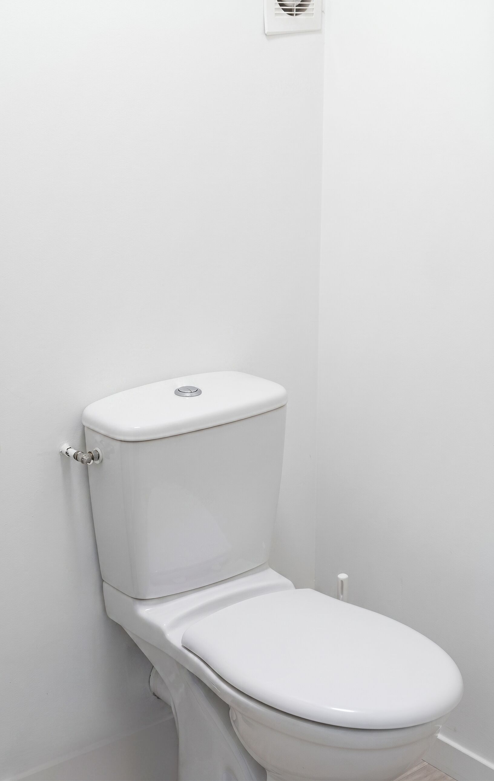A white toilet in a bathroom with a plain wall and a light switch above it.