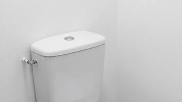 A white toilet in a bathroom with a plain wall and a light switch above it.