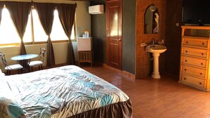 A hotel room with a bed, a small table with chairs, a sink, a mirror, and a television.