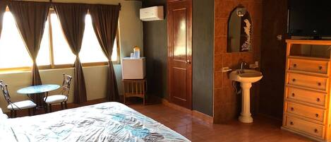 Une chambre d’hôtel comprenant un lit, une petite table avec des chaises, un lavabo, un miroir et un téléviseur.
