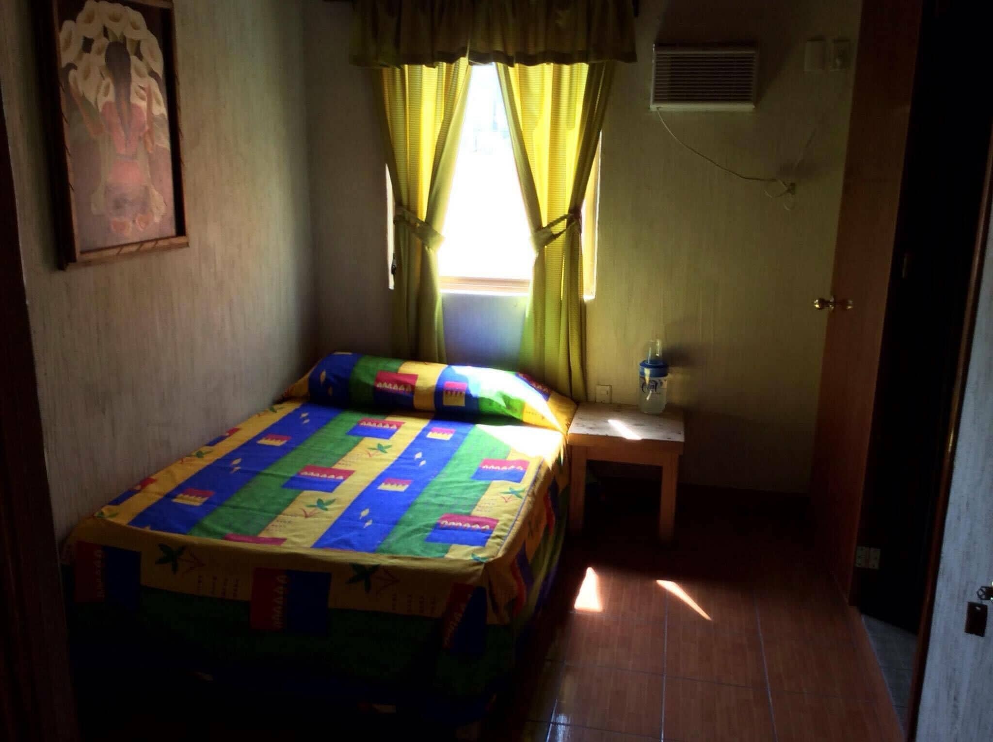 Una habitación pequeña y acogedora con una cama, una mesita de noche, una ventana con cortinas y un aire acondicionado de pared.