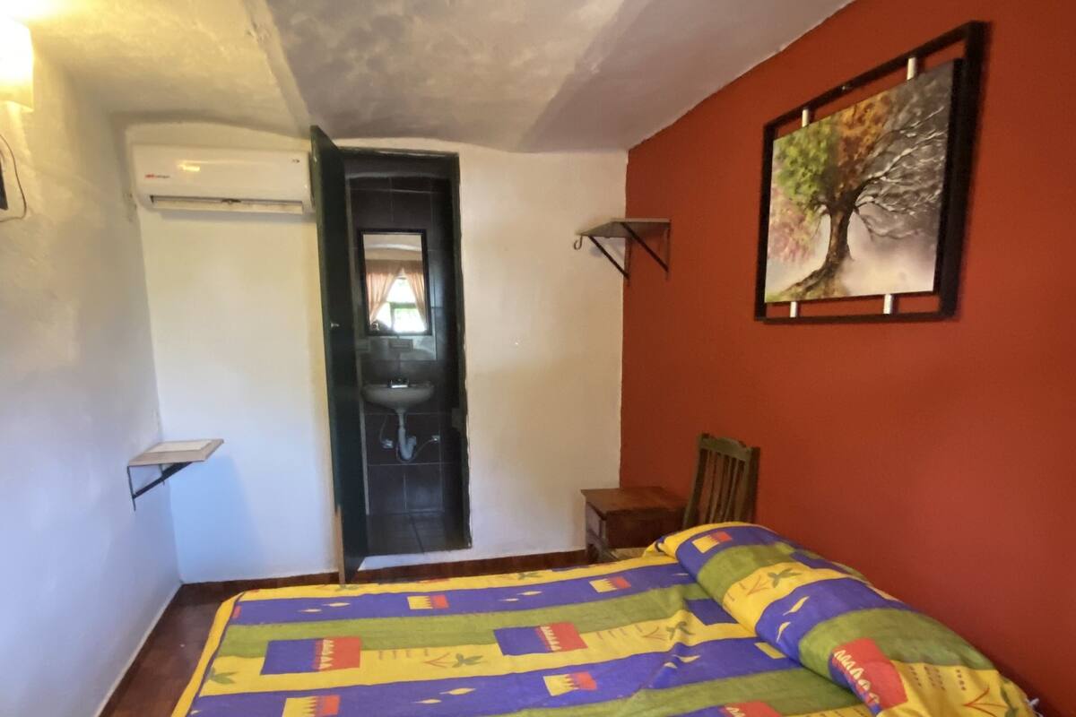 Een slaapkamer met een bed, een stoel, een deur en een wandplank.