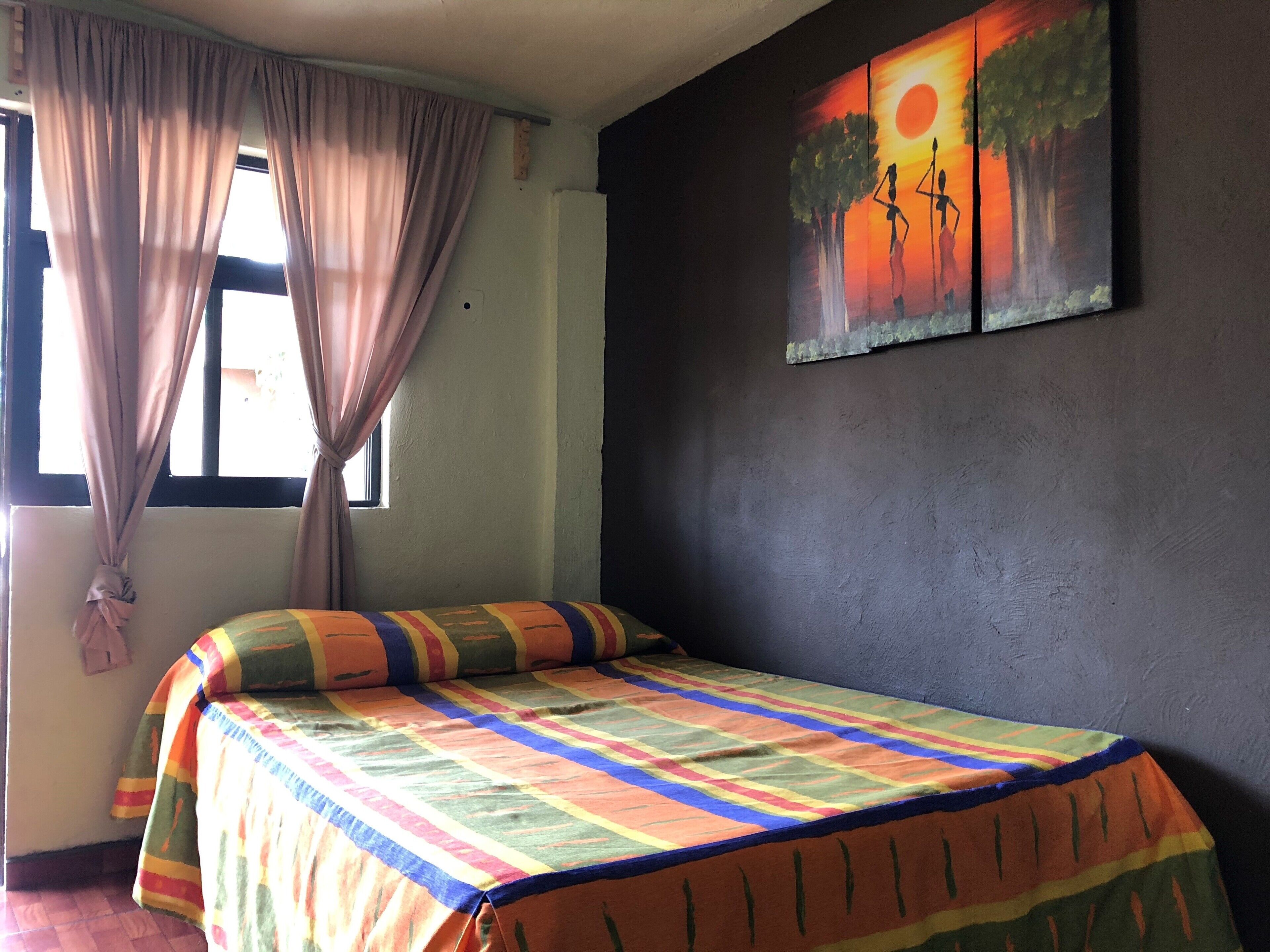 A bedroom with a bed, curtains, a window, and a wall painting.