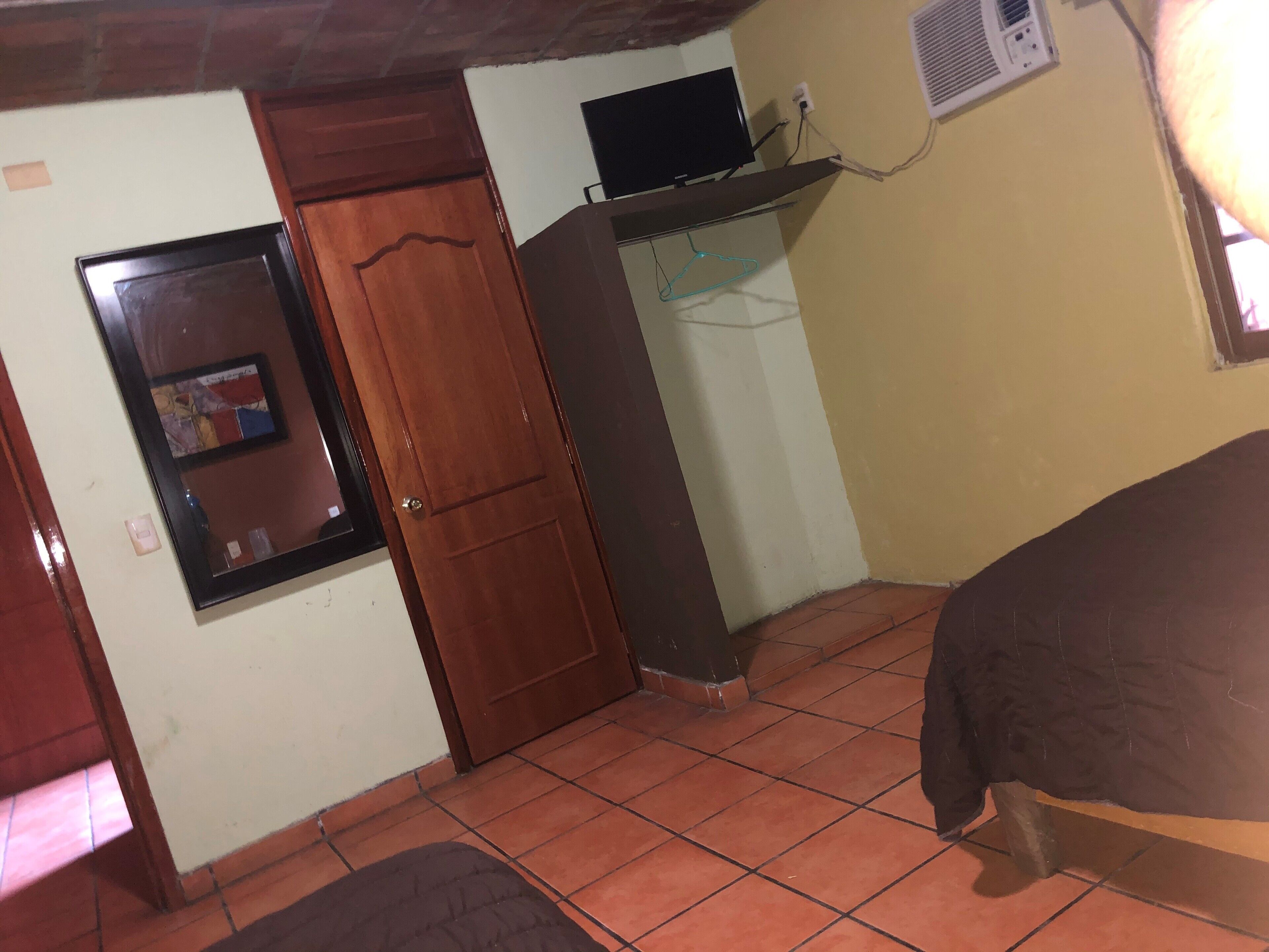 Une pièce avec une porte en bois, une petite fenêtre, un téléviseur fixé au mur et un lit.