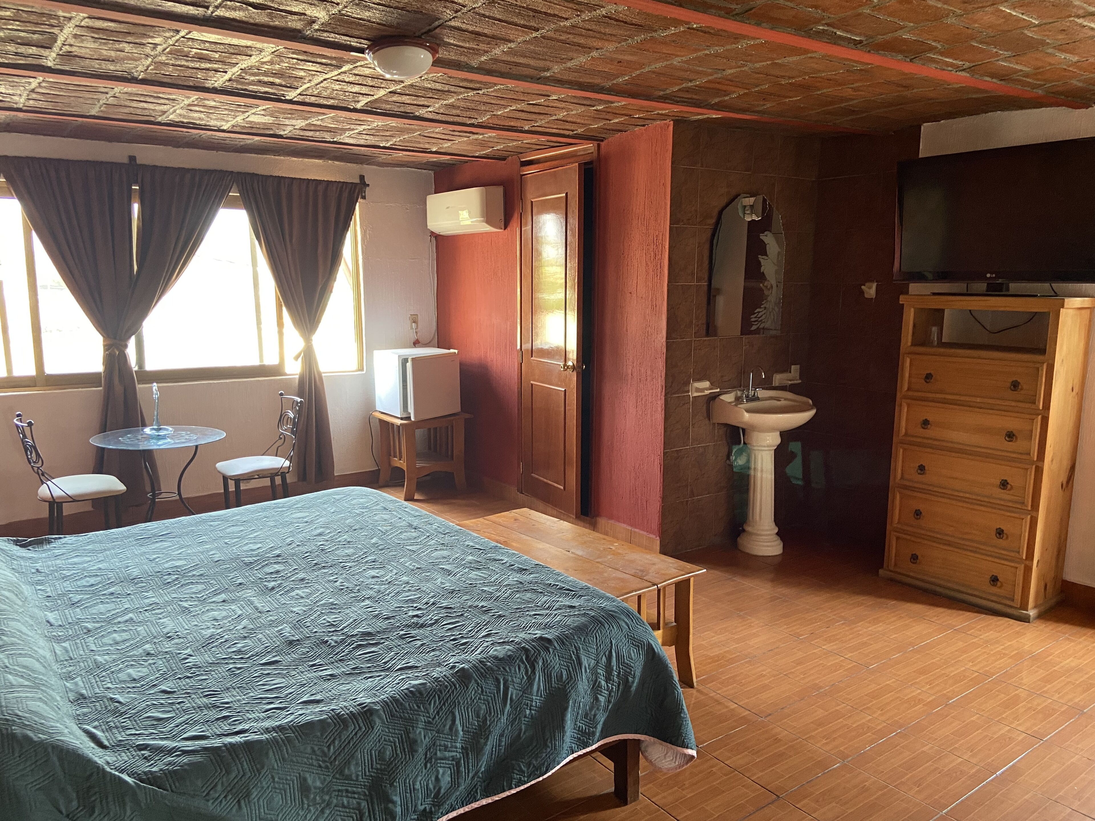 Una habitación con cama, una mesita, una silla, un lavamanos y un televisor.