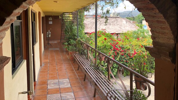 A covered balcony with a tiled floor, a bench, and a view of a garden with red flowers.