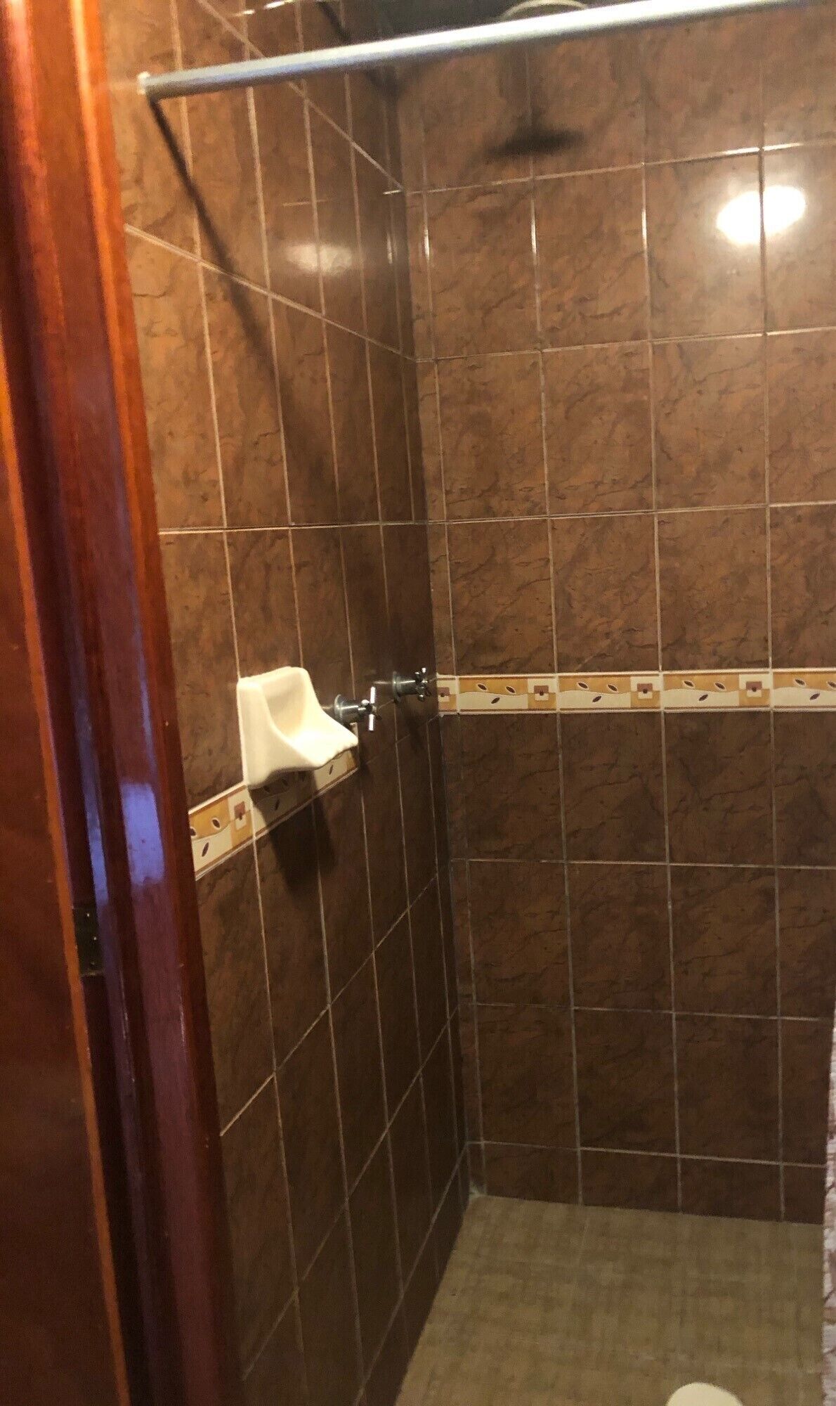 Un espacio de ducha con azulejos marrones, un lavabo blanco y un marco de puerta de madera.
