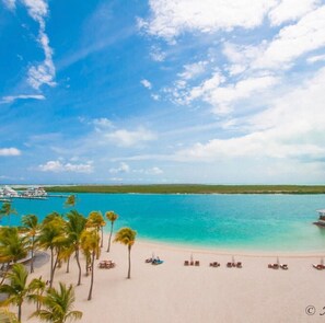 A beach with clear turquoise water, palm trees, and a dock with boats.