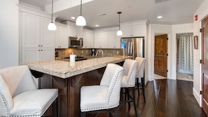 A modern kitchen with white cabinetry, a granite countertop, stainless steel appliances, and pendant lighting.