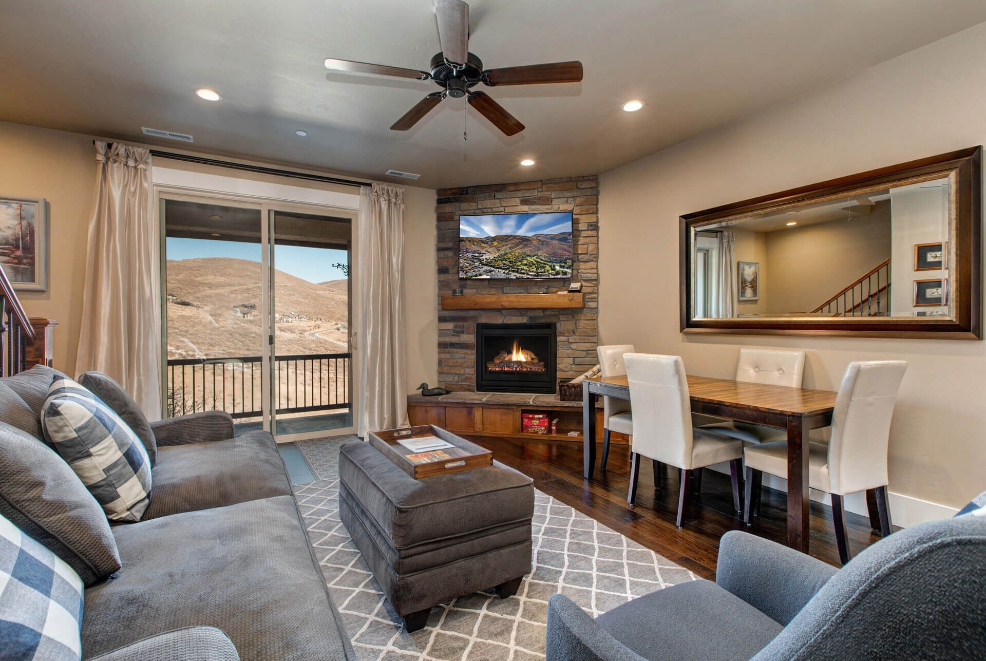 A living room with a fireplace, a dining area, and a balcony with a view of a mountainous landscape.
