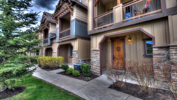 A multi-story residential building with a stone facade, multiple balconies, and a well-maintained front yard.