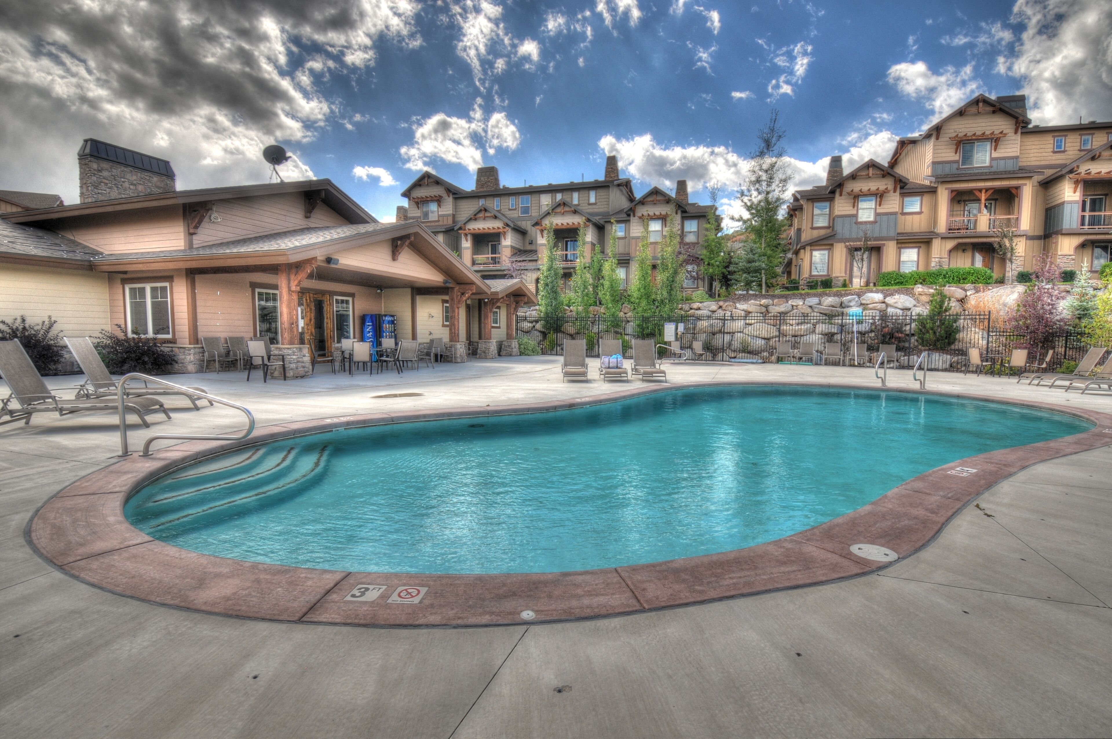 A swimming pool with lounge chairs and a building with multiple balconies in the background.
