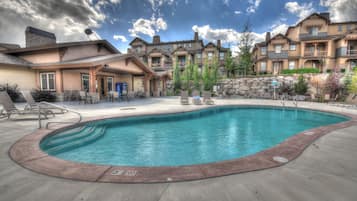 A swimming pool with lounge chairs and a building with multiple balconies in the background.
