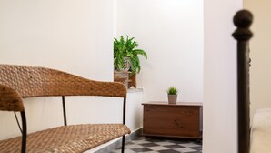 Un rincón de una habitación con una silla de mimbre, un aparador de madera y una planta en maceta.