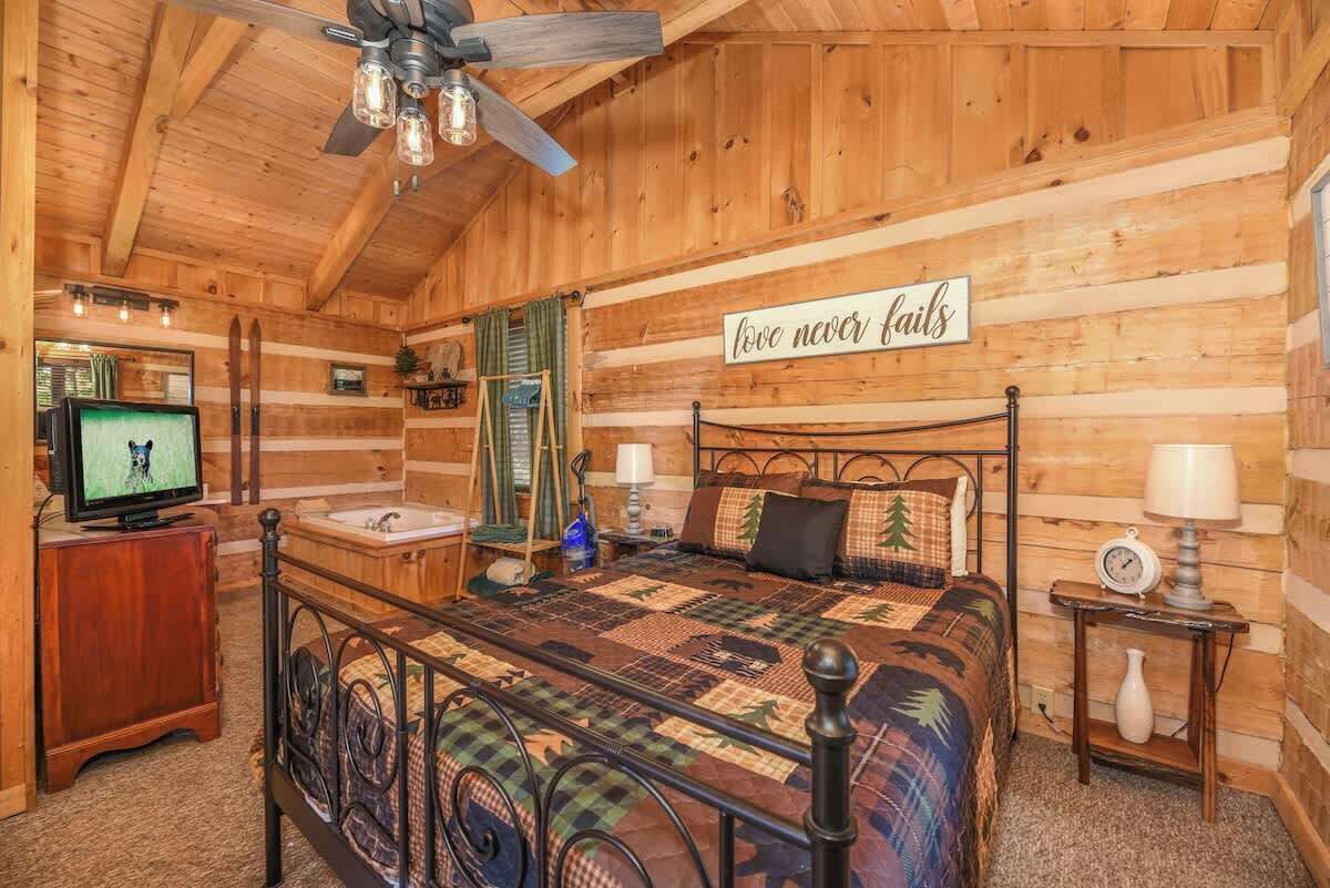 Ein gemütliches Schlafzimmer in einer Blockhütte mit Bett, Fernseher, kleinem Badezimmer und einem motivierenden Spruch an der Wand.