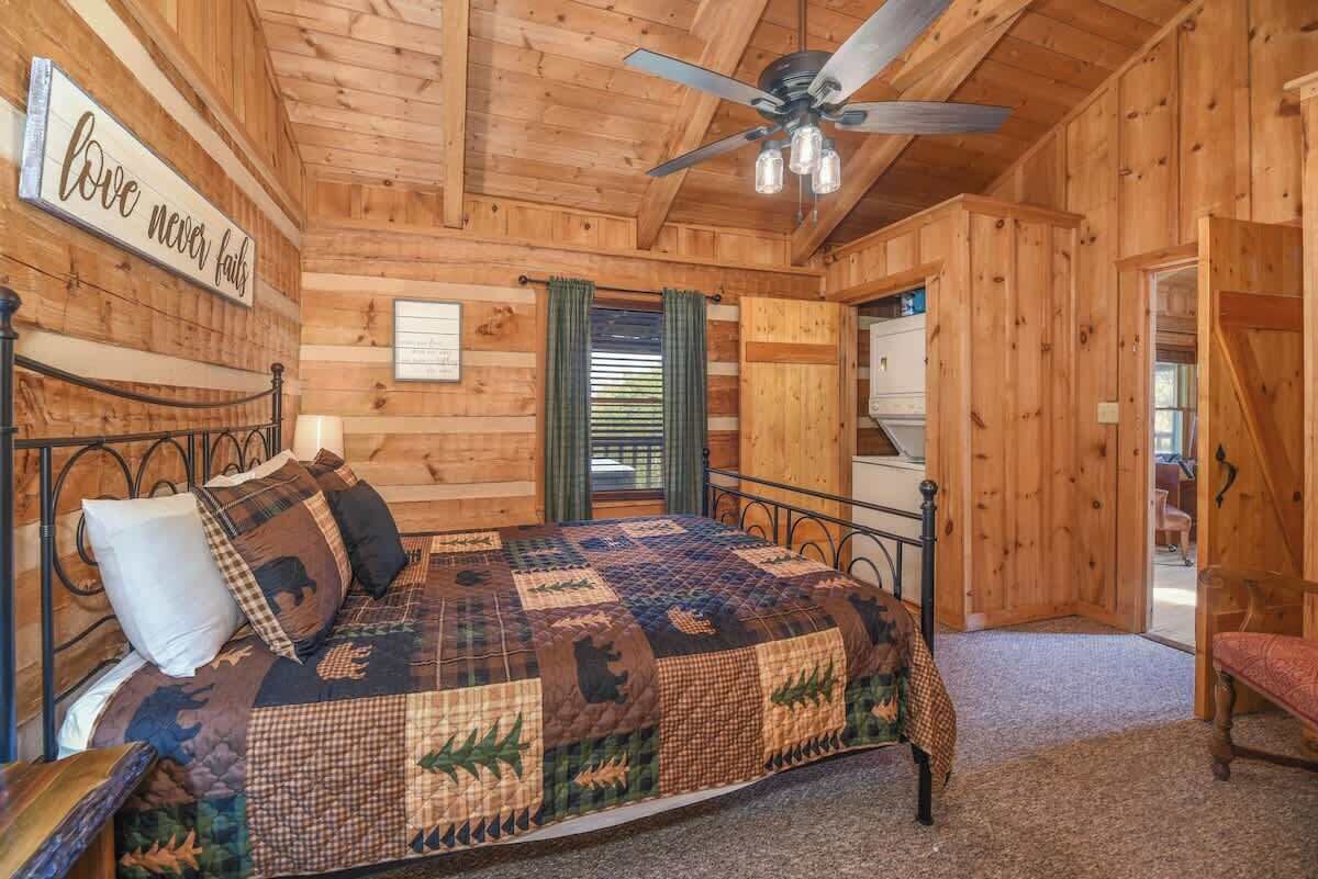 A wooden cabin bedroom with a bed, a ceiling fan, and a sign that reads "love never fails".