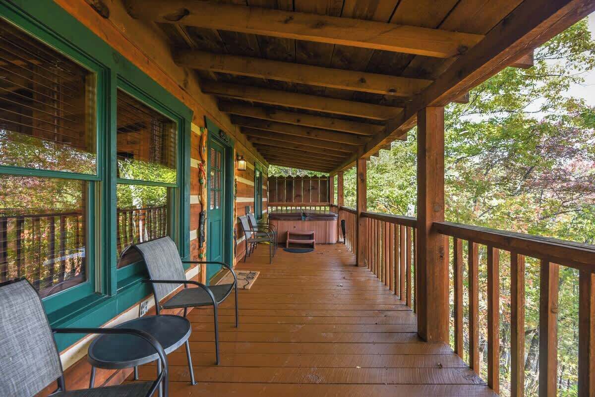 Een overdekt terras met houten leuningen, een jacuzzi en meerdere stoelen.
