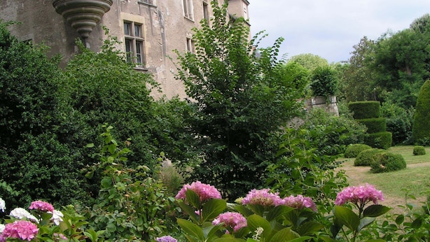 Un bâtiment historique doté d’une tour, entouré d’une végétation luxuriante et de plantes en fleurs.