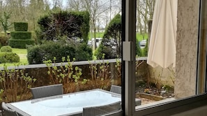 Une cuisine dotée d’un évier en acier inoxydable, d’une fen être donnant sur un jardin avec une table et des chaises de patio, et d’un parasol blanc sur le balcon.