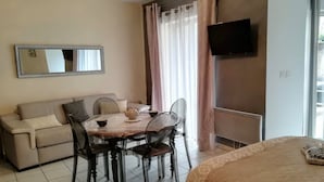 Une chambre d’hôtel équipée d’une table à manger, de chaises, d’un canapé, d’un téléviseur fixé au mur et d’une fenêtre avec des rideaux.