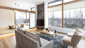 A modern living room with a fireplace, large windows, and a dining area with tatami mats.