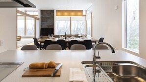 A modern kitchen with a dining area, large windows, and a stone fireplace.