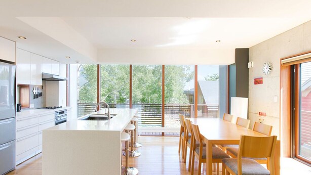 A modern kitchen with a central island, a dining area with wooden chairs, and large windows offering a view of the outdoors. - Luxury 3 Bed Ski Chalet in Prime Location, Niseko Chalet 1001 (Niseko)