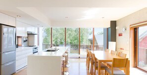 Una cocina moderna con una isla central, un comedor con sillas de madera y ventanas amplias que ofrecen vistas al exterior.