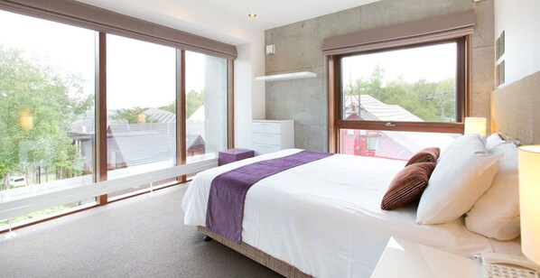 Un dormitorio moderno con una cama grande, una mesita de noche, un aparador y un ventanal con vistas al exterior.