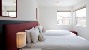 Ein Hotelzimmer mit zwei Betten, einem roten Kopfteil, einer Nachttischlampe und einem großen Spiegel.