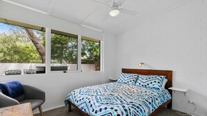 A bedroom with a bed, a chair, a window, and a ceiling fan.