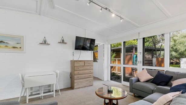 A spacious living room with a white brick wall, a wooden cabinet, a glass coffee table, and a grey sofa.