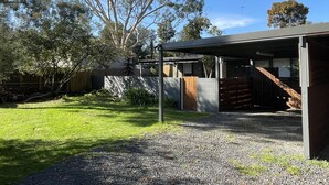 A modern house with a covered outdoor area, a gravel driveway, and a large tree in the yard.