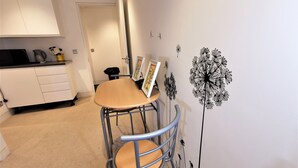 A small dining area with a table and chairs, a white cabinet, and a door in the background. - Spacious Double Room with en-suite - 1b (London)