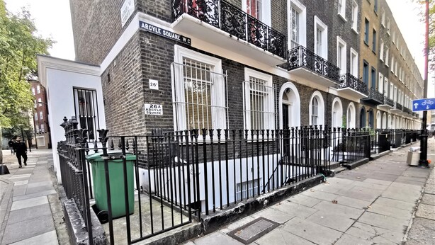 A row of terraced houses with black metal fences, a green trash bin, and a blue directional sign on the sidewalk. - Spacious Double Room with en-suite - 1b (London)
