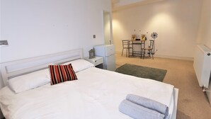 A bedroom with a bed, a nightstand, a desk with chairs, and a radiator. - Spacious Double Room with en-suite - 1b (London)