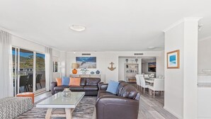 A spacious living area with a sofa, coffee table, and a dining table with chairs. There is a sliding glass door leading to an outdoor balcony.