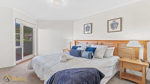 A bedroom with a bed, nightstands, a wooden headboard, a large window, and two framed artworks on the wall.