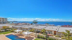 A resort with a swimming pool, outdoor seating, and a view of the ocean.