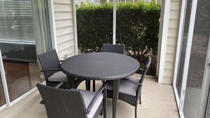A round outdoor table with wicker chairs, a glass door, and a hedge in the background. - Myrtle Beach Townhome on Legends Golf & Resort (Myrtle Beach)