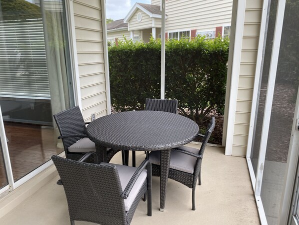 A round outdoor table with wicker chairs, a glass door, and a hedge in the background. - Myrtle Beach Townhome on Legends Golf & Resort (Myrtle Beach)
