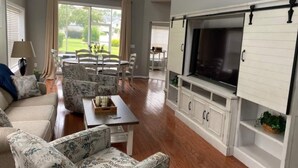 A spacious living room with a large TV, white cabinets, and a dining area with chairs and a table. - Myrtle Beach Townhome on Legends Golf & Resort (Myrtle Beach)