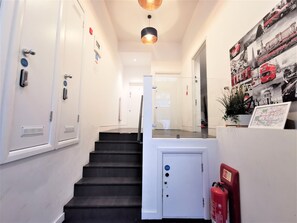 A hallway with a staircase, a fire extinguisher, and a wall-mounted map. - Spacious Double Room with en-suite - 2b (London)